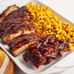 Succulent BBQ ribs with corn on a white platter, perfect for summer dinners or family feasts.
