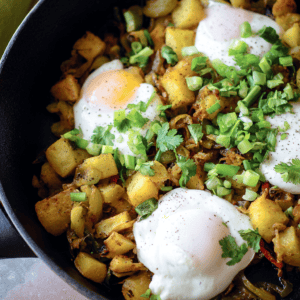 Scrambled eggs with potatoes, herbs, and green onions in a skillet.