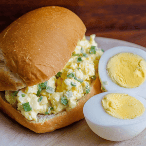 Scrambled eggs sandwich with chopped green onions on a toasted bun, served with half a boiled egg on the side.