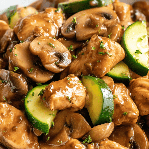 Sautéed chicken with mushrooms and zucchini, cooked in savory sauce, garnished with herbs.