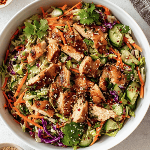 Fresh Asian-inspired chicken salad with mixed vegetables and sesame seeds in a white bowl.
