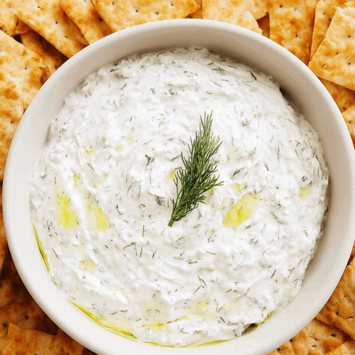Creamy dill yogurt dip garnished with fresh dill, served with crispy crackers for snack or appetizer.