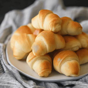 Fluffy homemade croissants on a white plate with a cloth napkin.