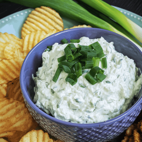 Creamy cucumber dip garnished with chopped green onions, served with potato chips and green onions. Perfect for snacks or parties.
