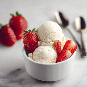Fresh strawberry ice cream with sliced strawberries in a white bowl on a marble surface.