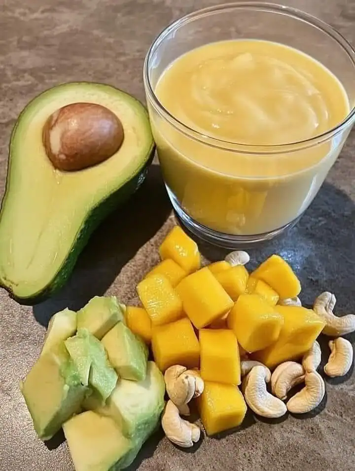 Creamy banana mango avocado smoothie in a glass with fresh fruits on the side