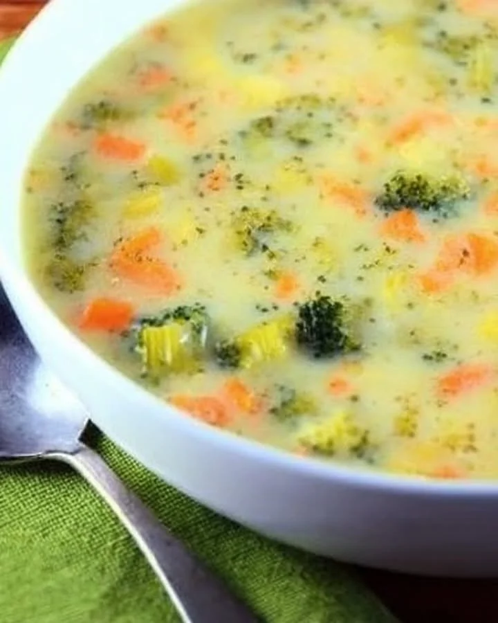 Bowl of broccoli cheese soup with cauliflower and garnished with herbs