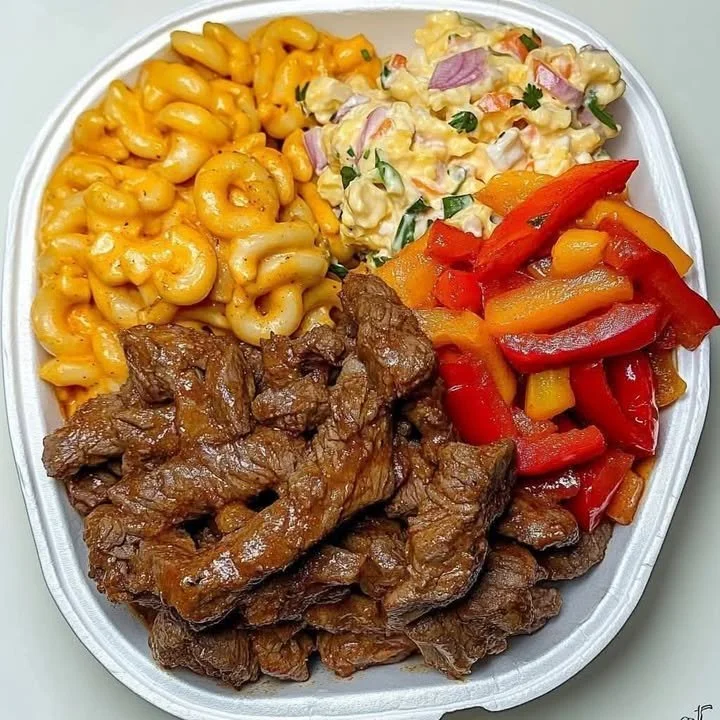 Plate of beef strips with macaroni and cheese, potato salad, and sautéed bell peppers.